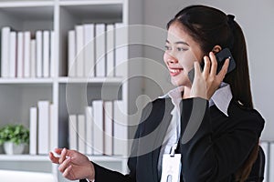 Successful Asian businesswoman sitting in modern office Use a phone and laptop to calculate tax and finance.