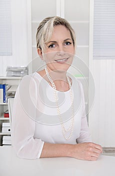 Successful attractive blond older businesswoman sitting at desk.