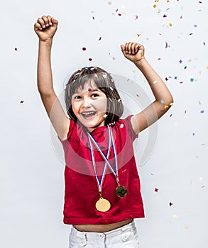 Successful beautiful child laughing with champion medals, celebrating over confettis