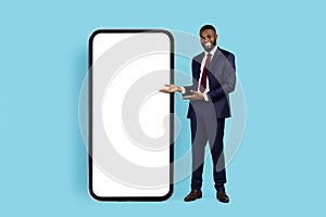 Successful Black Businessman Pointing At Big Smartphone With White Blank Screen