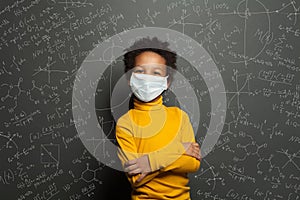 Successful black child boy student in protective face mask on black chalkboard background