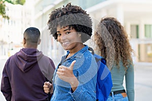 Successful black female student with backpack and friends showing thumb up