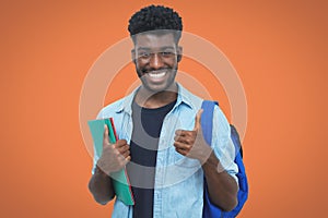 Successful black male student with beard showing thumb up on orange background