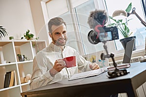 Successful blogger. Portrait of smiling male blogger drinking a tea while making a new video at home.