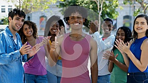 Successful brazilian male young adult showing thumb up with group of applauding people
