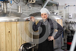 Successful brewer standing in brewery near fermentation tanks