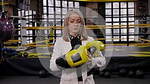 A successful business lady in a white business suit puts on boxing gloves.