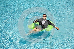 Successful business man floating in suit in pool water. Summer vacations and travel concept. Funny business man drink