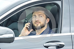 Successful business man with a phone in his hand sits behind the wheel of a prestigious car