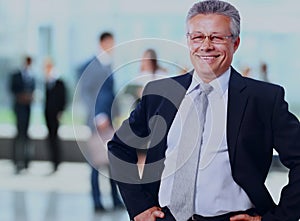 Successful business man standing with his staff in background at office.