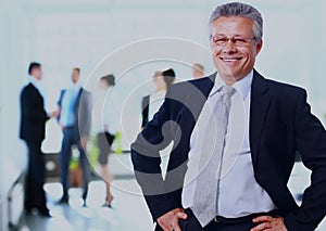 Successful business man standing with his staff in background at office.