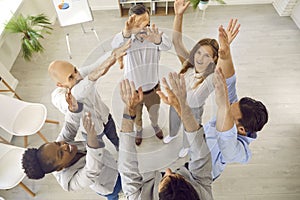 Successful business people on corporate team building training standing with hands up in office.