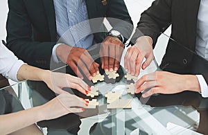 Successful business team folding the pieces of the puzzle sitting behind a Desk