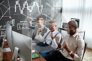 Successful business team. Three stock traders looking at graphs, indexes and numbers on multiple computer screens