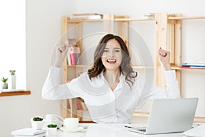 Successful business woman with arms up sitting in modern office.