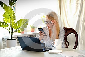 Successful business woman looking at mobile phone while at home in office work space