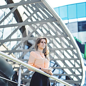 Successful business woman standing on the balcony of the modern office and looks into the distance.