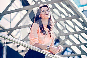 Successful business woman standing on the balcony of the modern office and looks into the distance.