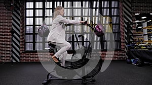 A successful business woman in a white business suit trains on an exercise bike.