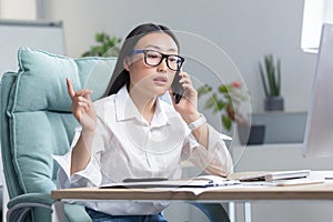 Successful business woman working in modern office, Asian woman talking on the phone, female worker wearing white shirt