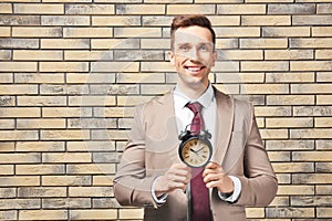 Successful businessman with alarm clock against brick wall. Time management concept