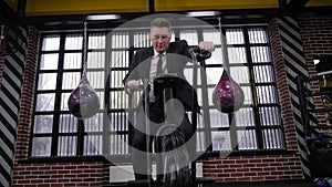 A successful businessman in a black suit trains on a bicycle in a boxing gym.