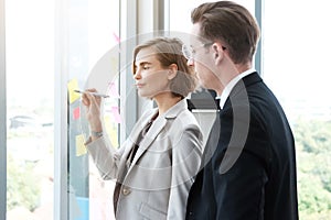 Successful businessman and businesswoman writing good ideas on sticky notes pasted on glass wall  in modern office.