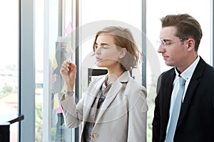 Successful businessman and businesswoman writing good ideas on sticky notes pasted on glass wall  in modern office.