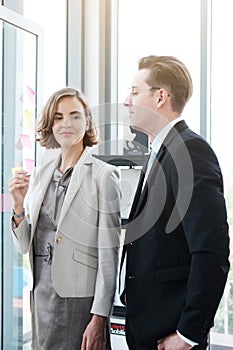 Successful businessman and businesswoman writing good ideas on sticky notes pasted on glass wall  in modern office.