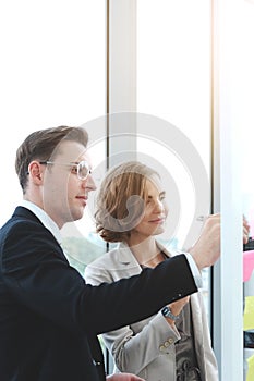 Successful businessman and businesswoman writing good ideas on sticky notes pasted on glass wall  in modern office meeting