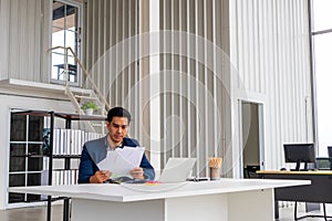 Successful businessman holding document sitting at desk, reading good news in letter, reviewing beneficial lucrative