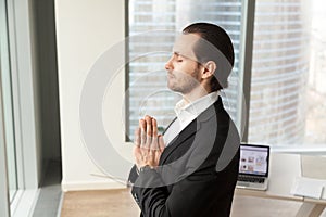 Successful businessman meditating at workplace in modern office.
