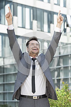 Successful businessman pointing upwards outside office building