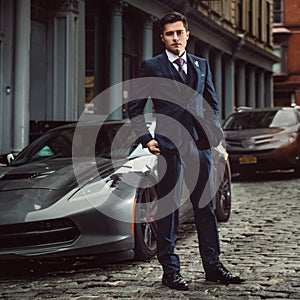 Successful businessman posing with a luxury sports car in New York City street.