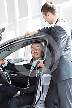 Successful businessman, receiving the keys to the car from the seller in the showroom
