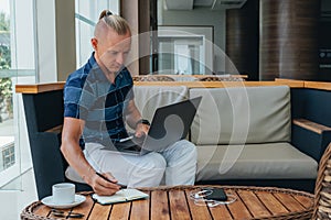 A successful businessman in a shirt and trousers is in a cafe, busy with remote work using modern technology. Works with laptop