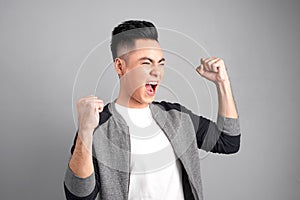 Successful businessman shouting with arms up suggesting his fulfillment, isolated on gray background