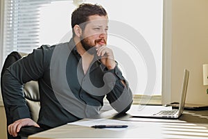 Successful businessman sitting at office desk working on laptop computer.