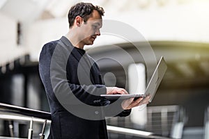 Successful businessman standing in office center holding laptop