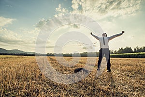 Successful businessman standing victoriously in the middle of field