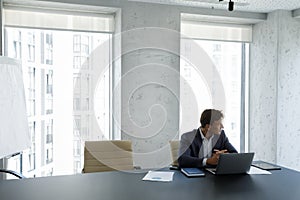 Successful businessman staring out window seated at modern skyscraper office