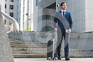 successful businessman in stylish suit with luggage and flight tickets going down stairs
