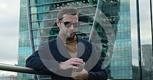 a successful businessman in a suit stands near a skyscraper and counts money