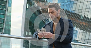 a successful businessman in a suit stands near a skyscraper and counts money