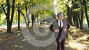 Successful businessman in sunglasses and suit dances and jumps in a autumn Park.