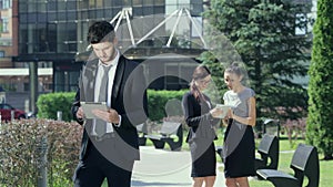 Successful businessman with tablet stands on the background of two businesswomen