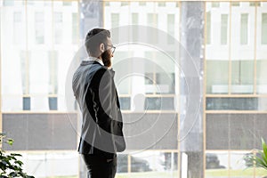 Successful businessman talking on phone, standing near window in office