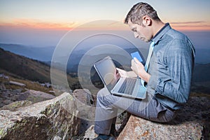 Successful businessman on top of mountain, using a laptop