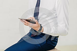 Successful businessman in white shirt, black trousers, tie holds tablet, checks notification.  on white background