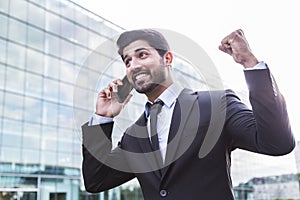 Successful businessman or worker in suit with phone near office building